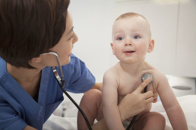 Smiling Doctor Checking A Baby S Heart Beat With A Stethoscope In The Doctors Office